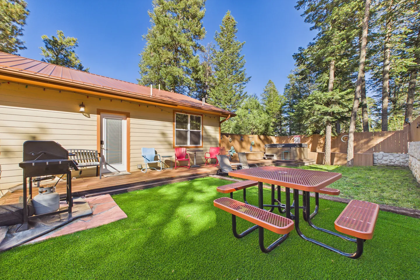 Fenced backyard featuring an artificial turf lawn, picnic table, barbecue grill, back porch, and hot tub.