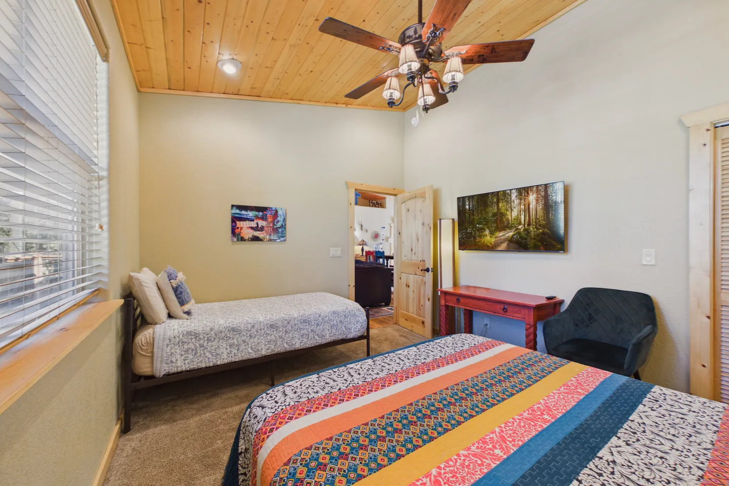 Bedroom with wood-paneled ceiling, ceiling fan, twin bed along the wall, and larger bed in the foreground.