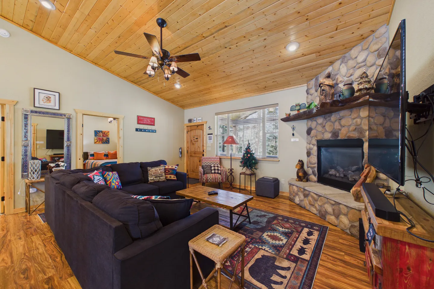 Living room featuring wood-paneled angled ceiling, stone fireplace, sectional sofa, and wood-look flooring.