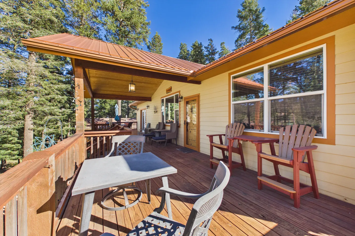 Spacious wooden deck with outdoor seating, a table, and partial roof overhang surrounded by pine trees.