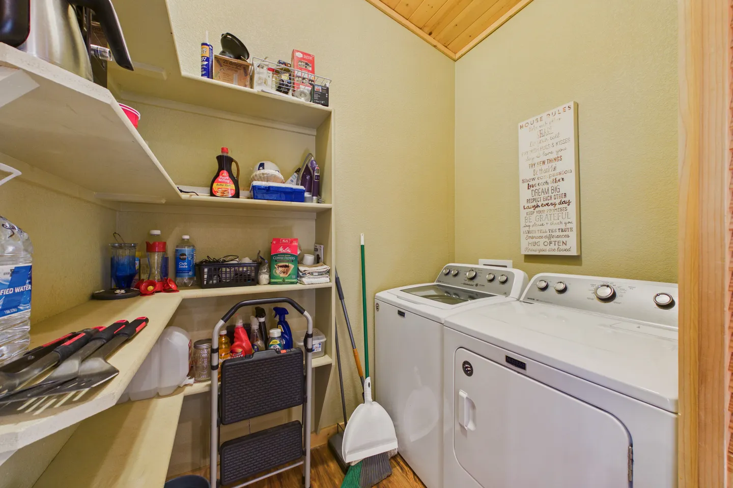 Laundry room and pantry area with a white washer, dryer, and multi-tier shelving stocked with household items.