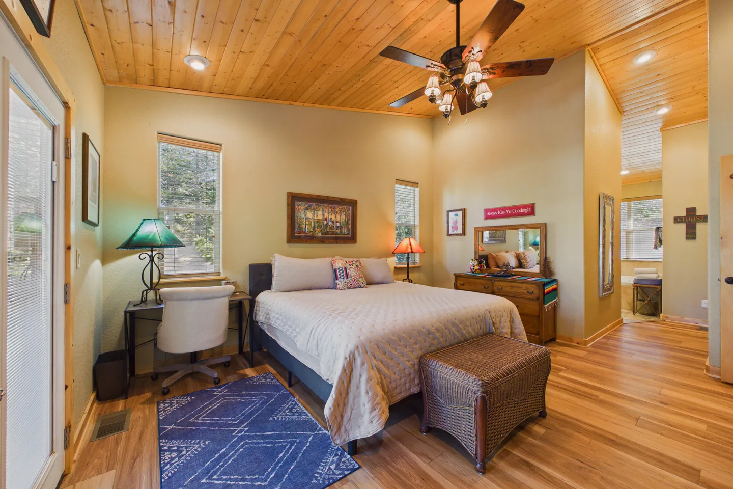 Bedroom with a wood-plank ceiling, ceiling fan, bed, wicker chest, small desk with chair, and wood-look flooring.