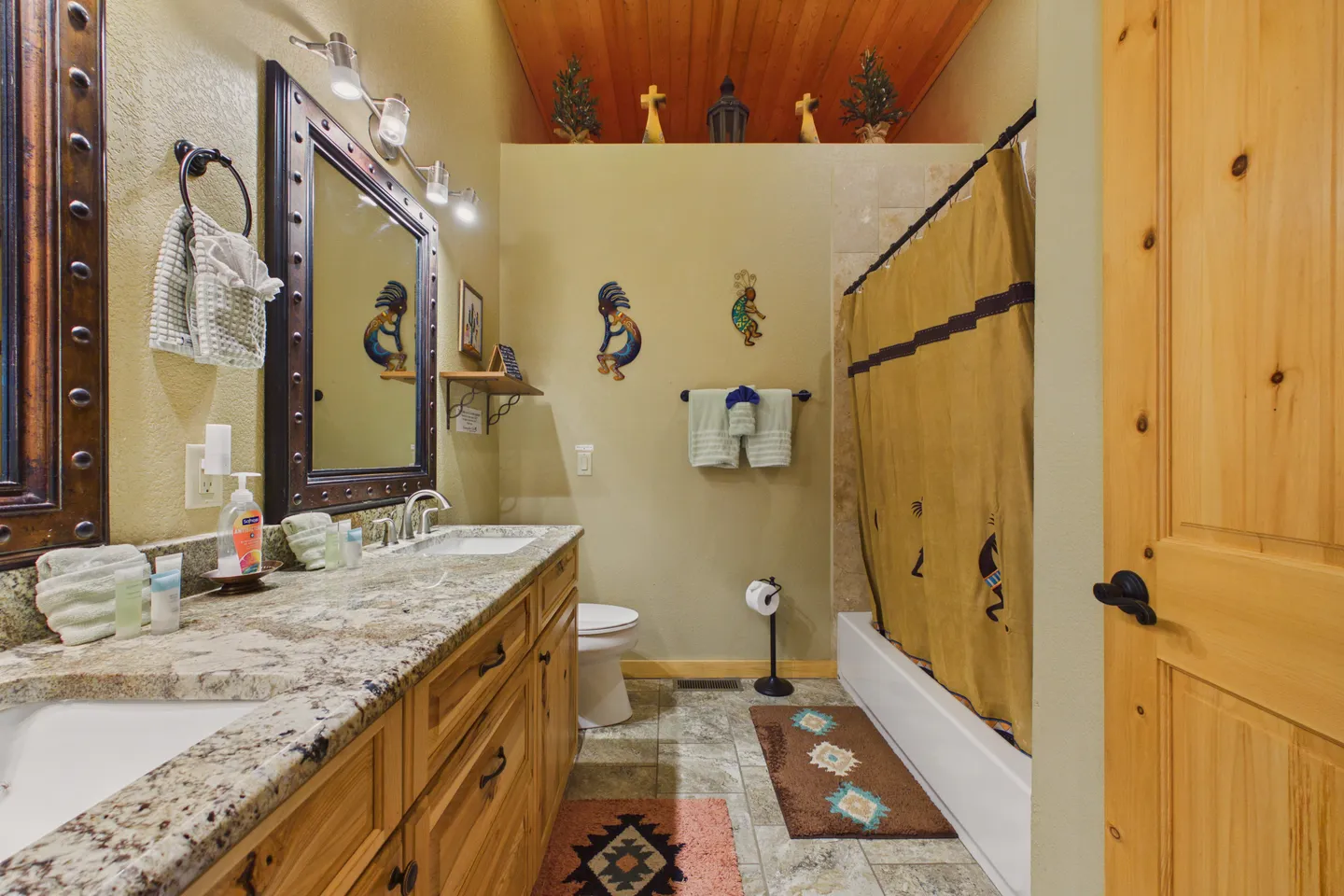 Bathroom with a double vanity, large mirror, toilet, bathtub and shower combination, and Southwestern-themed decor.