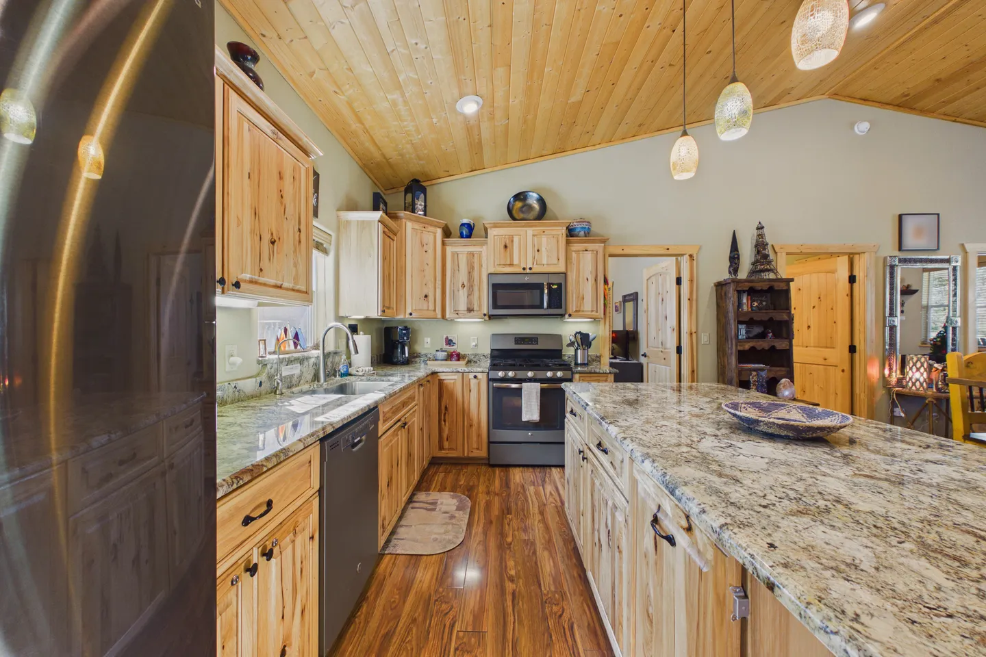 Kitchen with knotty wood cabinetry, granite countertops, kitchen island, and a wood-paneled vaulted ceiling.