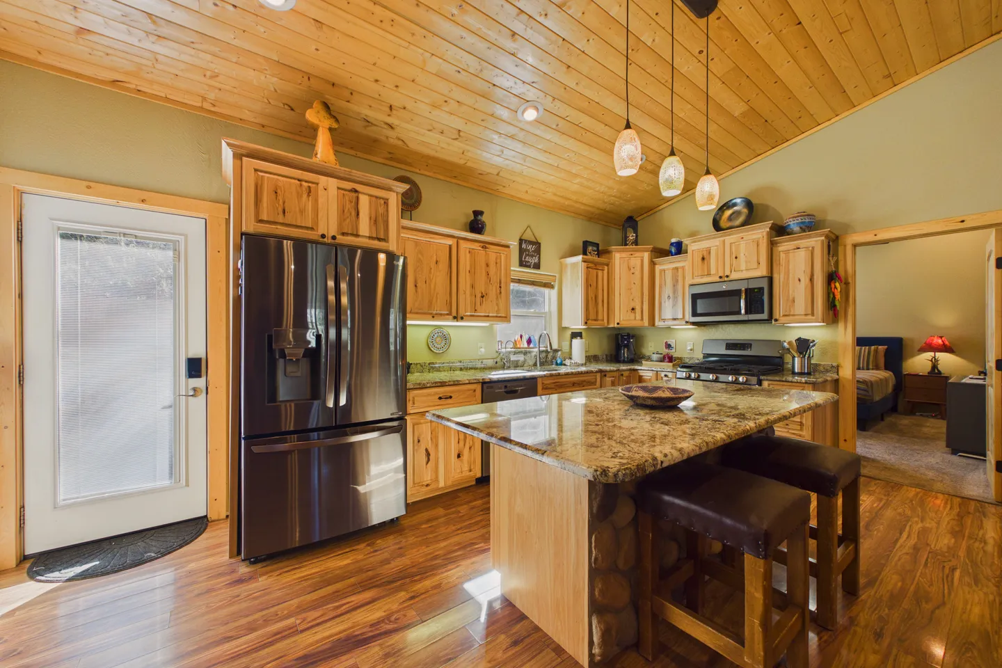 Kitchen with wooden cabinetry, stainless steel appliances, a wood-paneled ceiling, and an island with barstools.