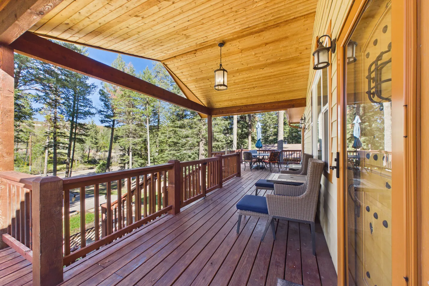 A long, covered wooden deck with seating overlooks a pine forest on a bright sunny day.