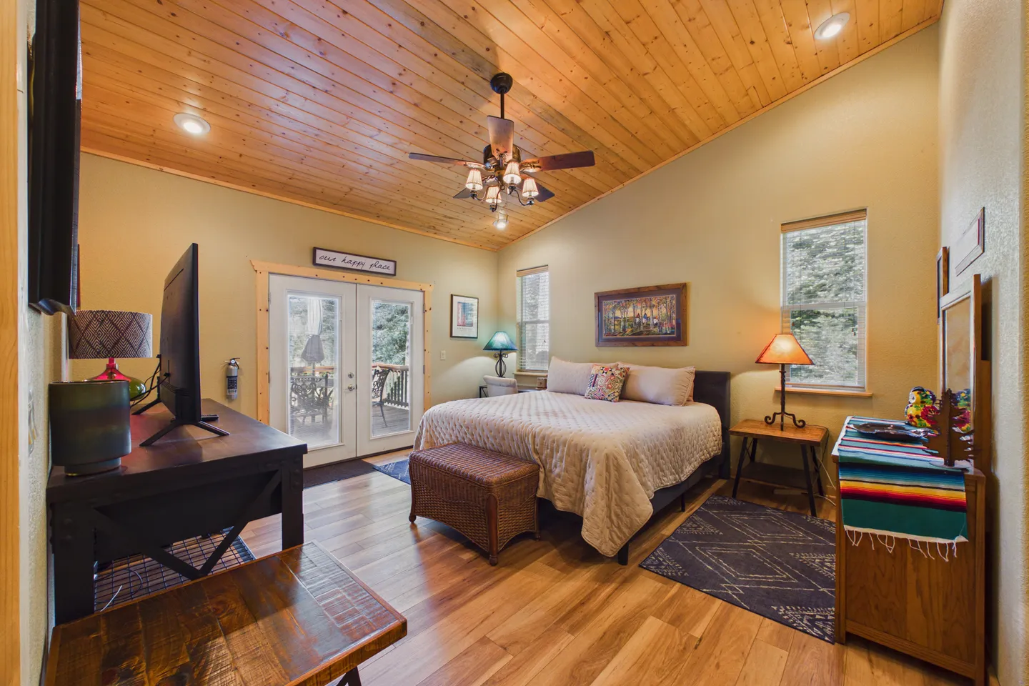Bedroom with a wood-plank vaulted ceiling, wood-look flooring, a bed, a dresser, a desk with a TV, and glass doors leading to an outdoor deck.