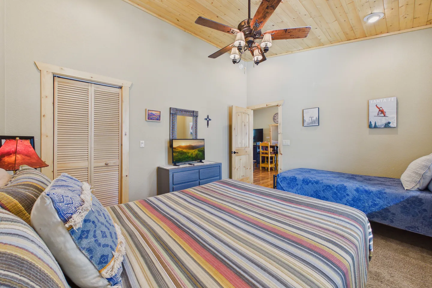Bedroom with wood-paneled ceiling, ceiling fan, main bed with striped bedding, a daybed, and a television on a blue dresser.