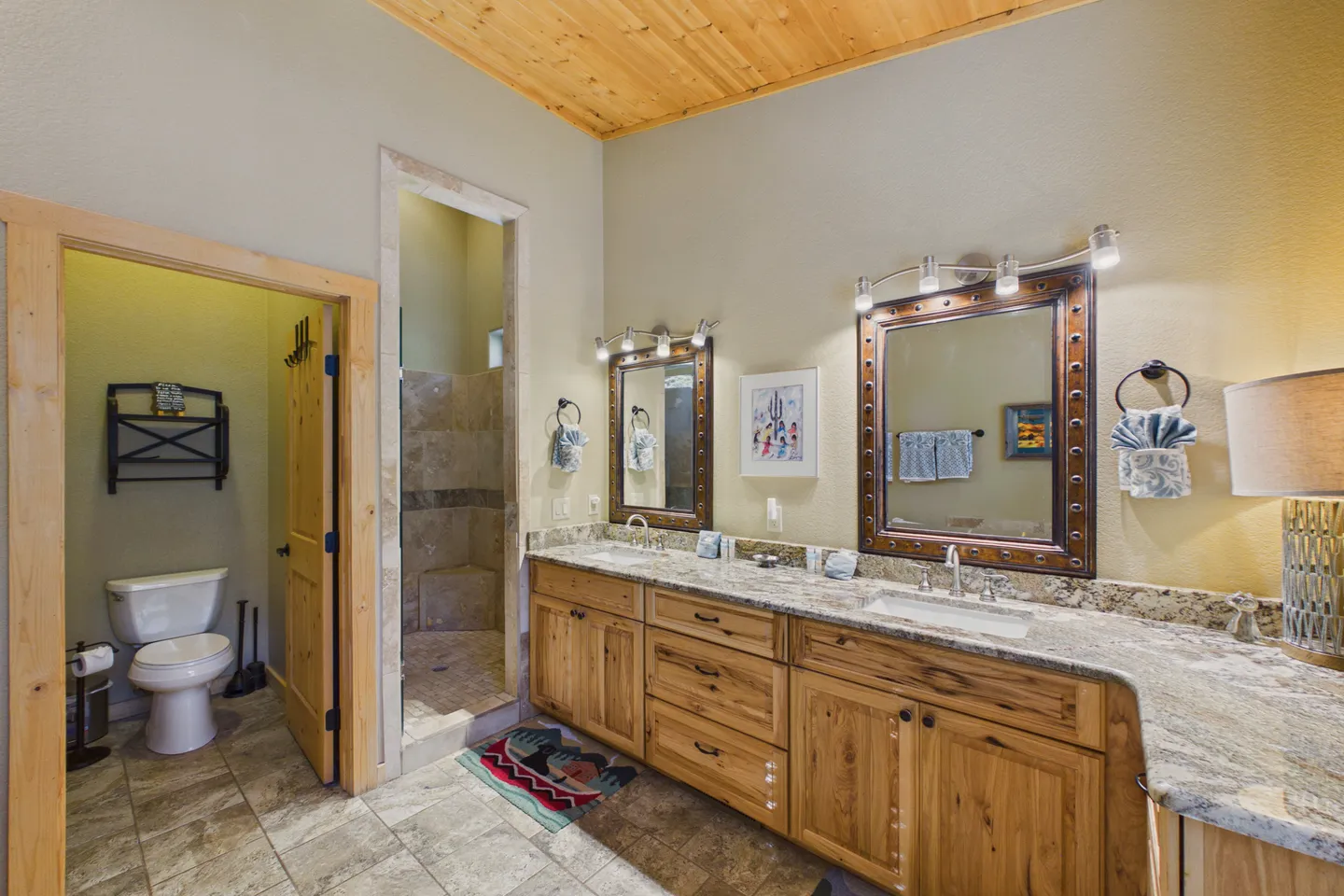 Primary bathroom featuring a double vanity with wooden cabinets, dual framed mirrors, a walk-in shower, and an enclosed toilet room.