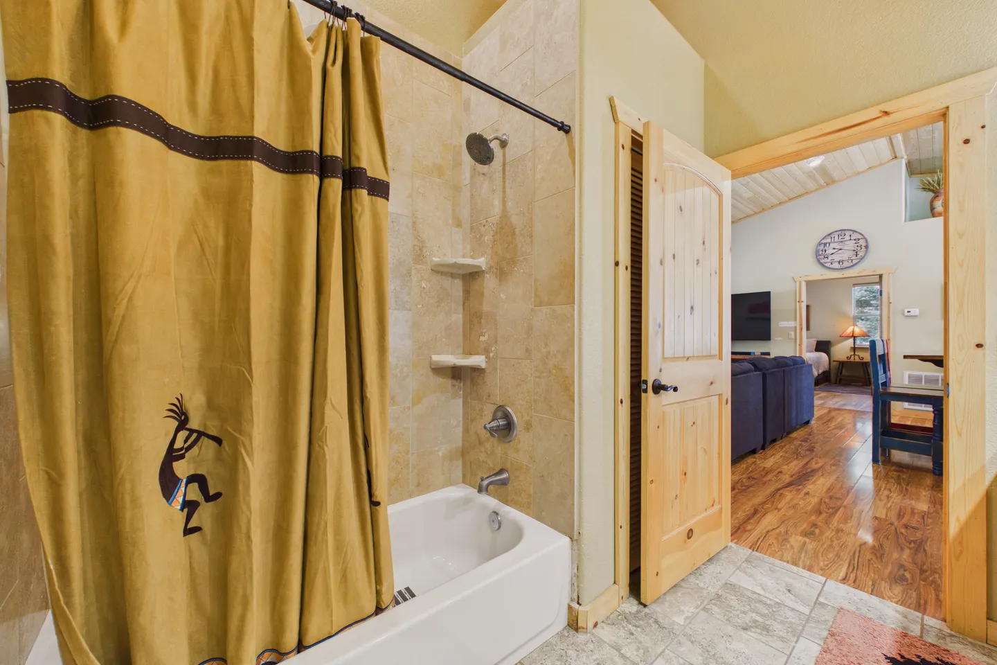 Bathroom with a bathtub, shower head, tiled walls, Kokopelli shower curtain, and an open pine door leading to the living area.