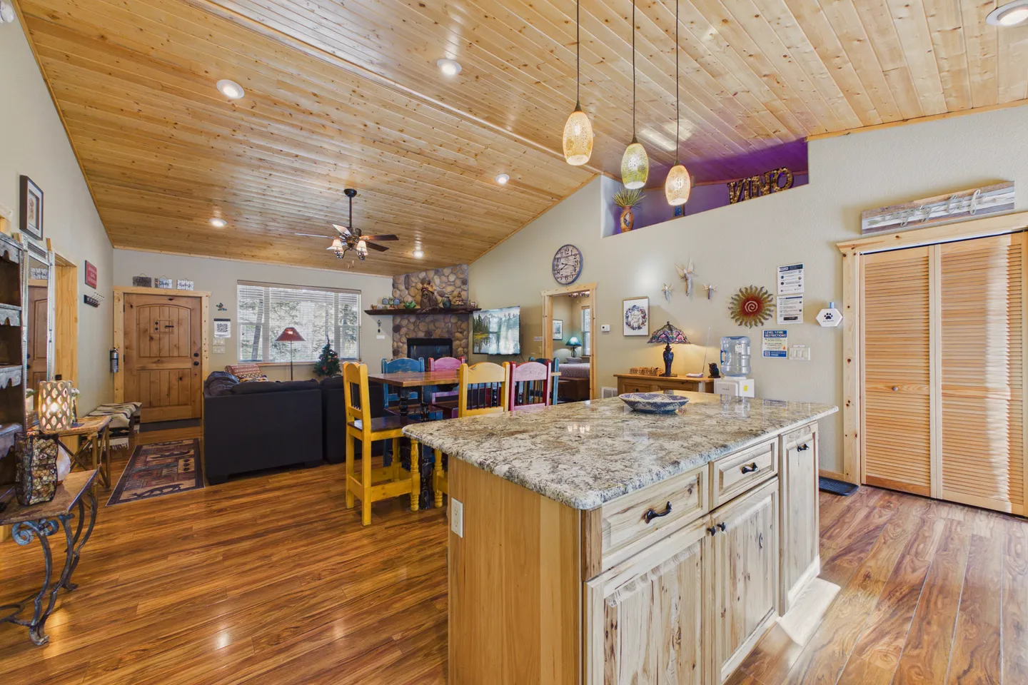 Open-concept living and dining area viewed from a kitchen island, featuring wood-paneled vaulted ceilings and wood floors.