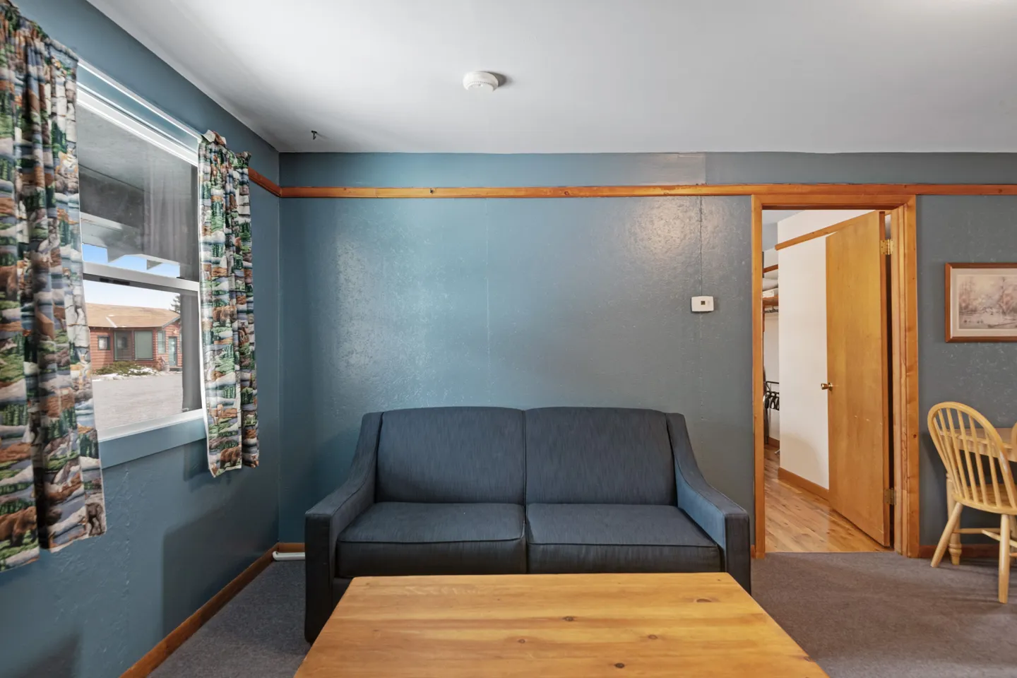 Living room interior featuring a blue sofa, wooden coffee table, patterned curtains on a window, and blue-gray painted walls.