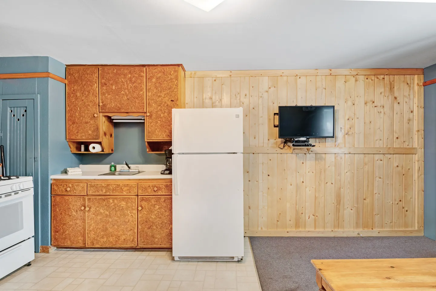 Kitchenette with wooden cabinetry, white refrigerator, and a wall-mounted TV on vertical wood paneling.