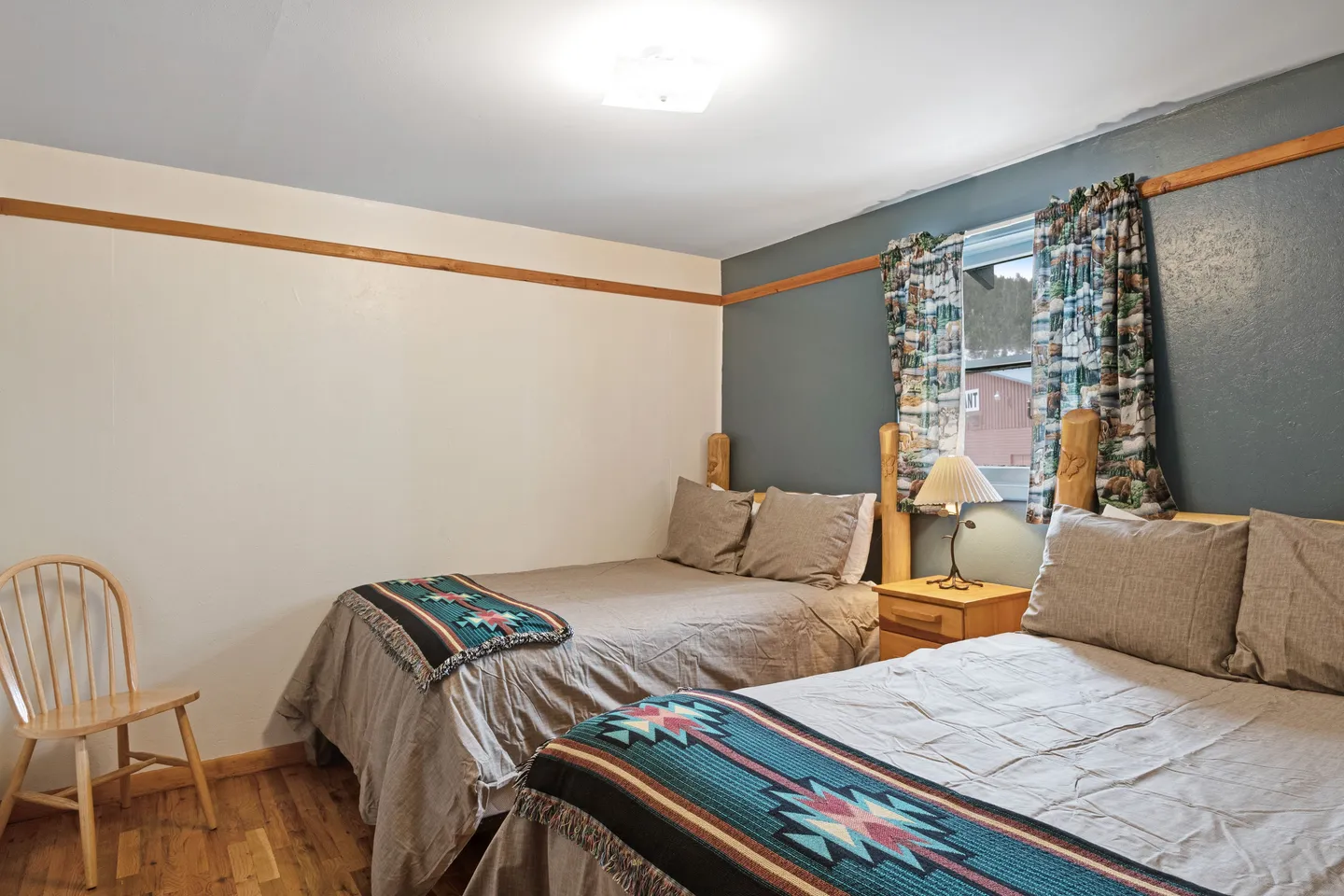 Bedroom with two beds made up in grey linens and Southwestern-patterned runners, separated by a nightstand with a lamp.