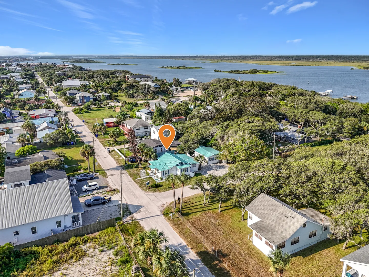 Aerial view of a coastal neighborhood featuring a home with a bright turquoise roof highlighted by a location pin near a bay.