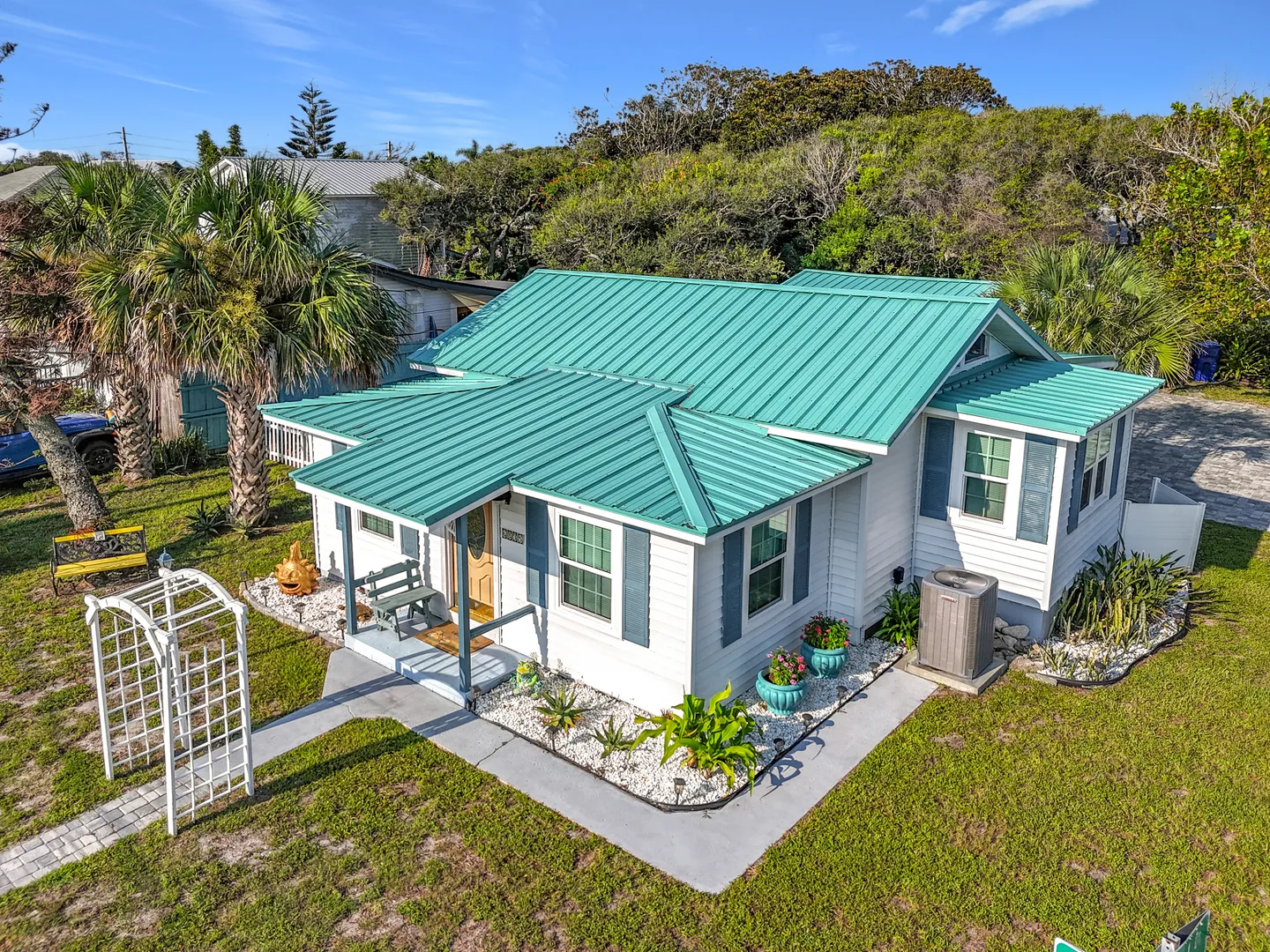 Elevated view of a white cottage with a teal metal roof, matching shutters, and front yard landscaping.