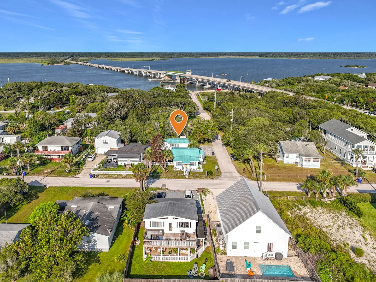 Aerial view of a coastal neighborhood featuring houses near a body of water and a long bridge under a clear sky.
