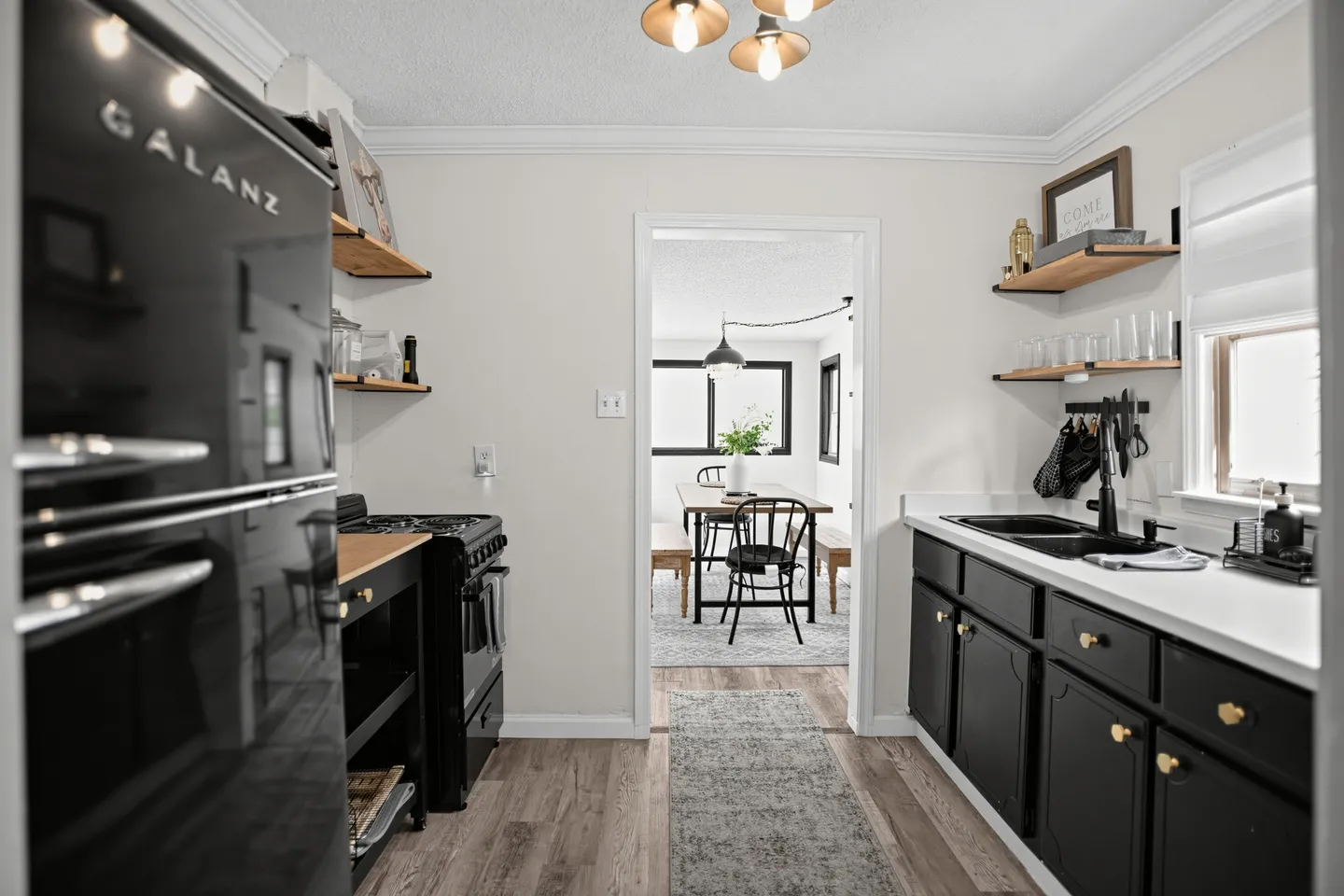 Kitchen with black cabinets, open shelving, black appliances, and a doorway looking into an adjacent dining area.