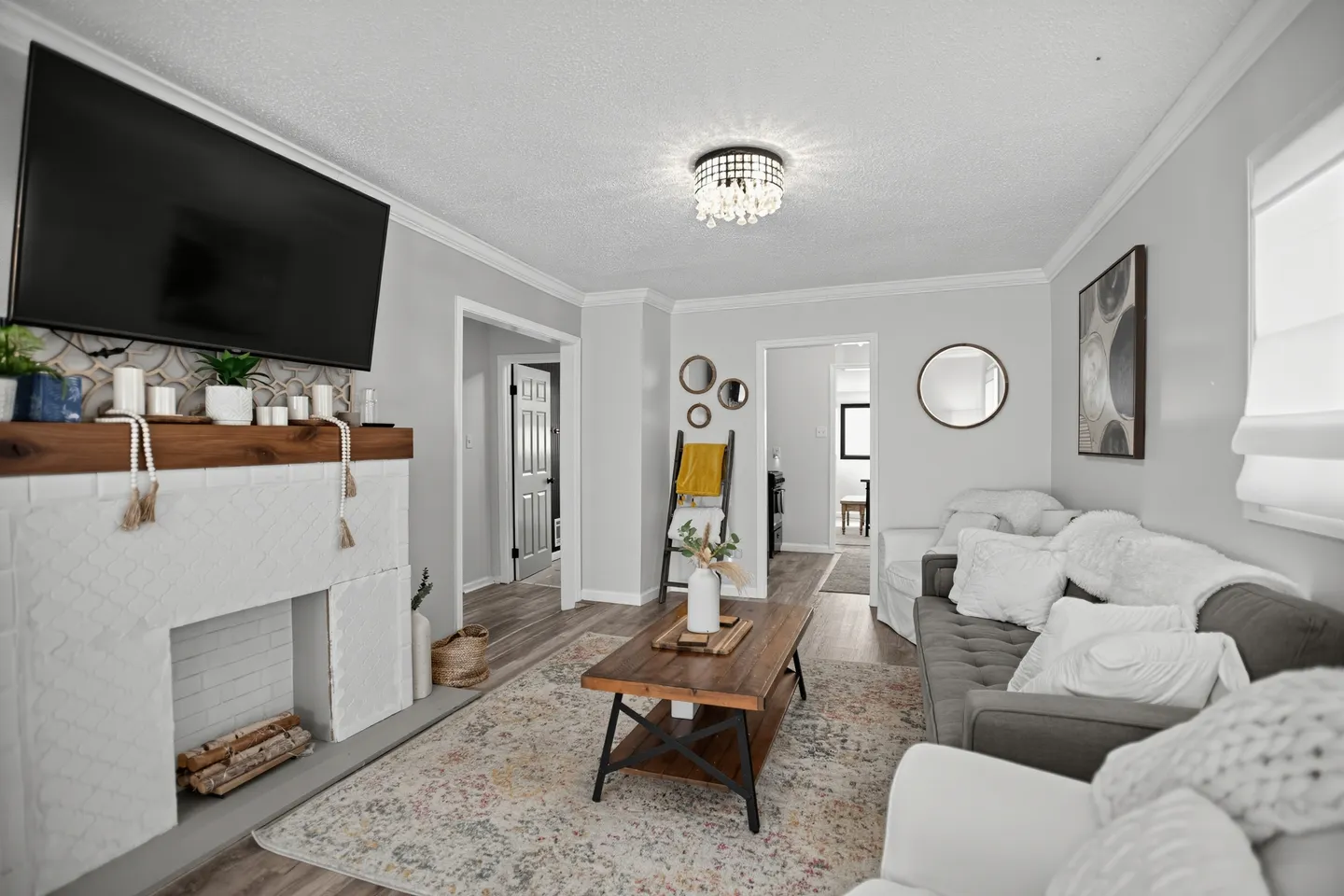 Living room featuring a light gray couch with pillows, a rustic coffee table on an area rug, and a fireplace mantle below a mounted television.