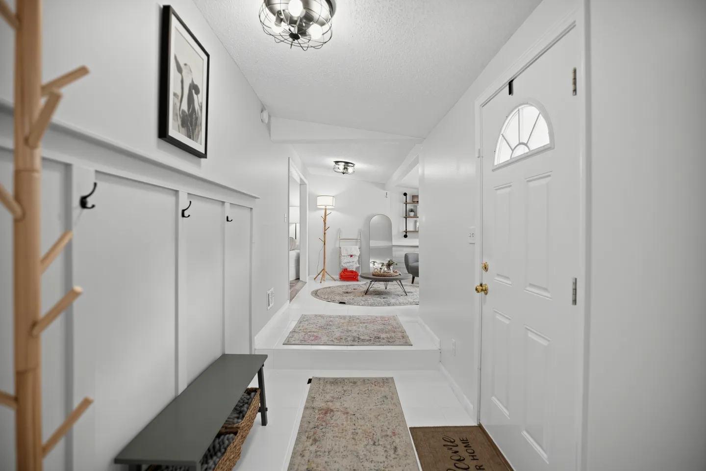 Front entryway with white walls, coat hooks, a bench, and a sunken hallway leading up a step to a living area.