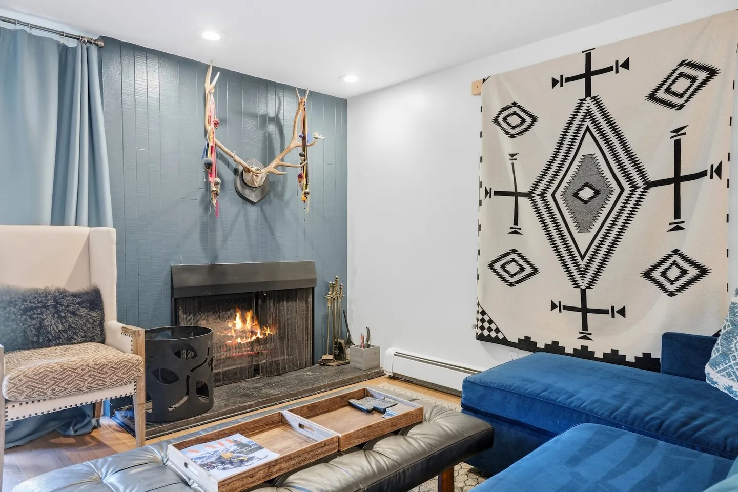 Living room with a lit fireplace, blue wood-paneled accent wall, antler decor, and a blue sectional sofa.
