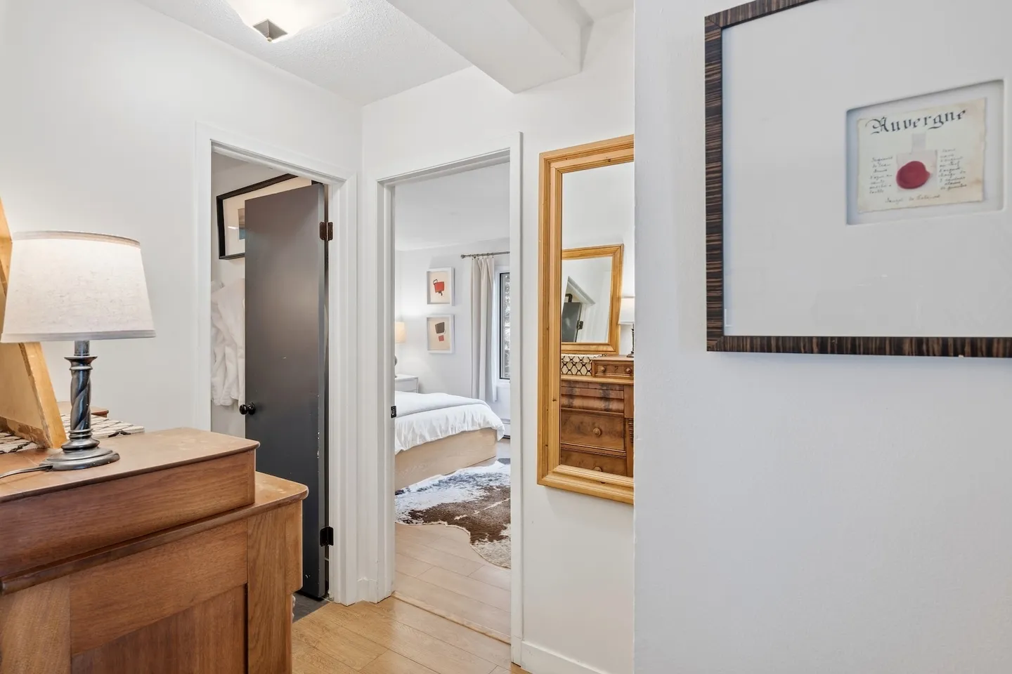 Hallway featuring a wooden dresser with a lamp, a framed mirror, and doorways leading to a bathroom and a bedroom.