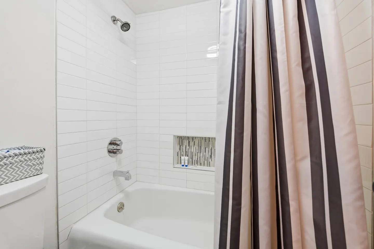 Bathroom shower and tub combination featuring white subway tile, a recessed niche, chrome fixtures, and a striped shower curtain.