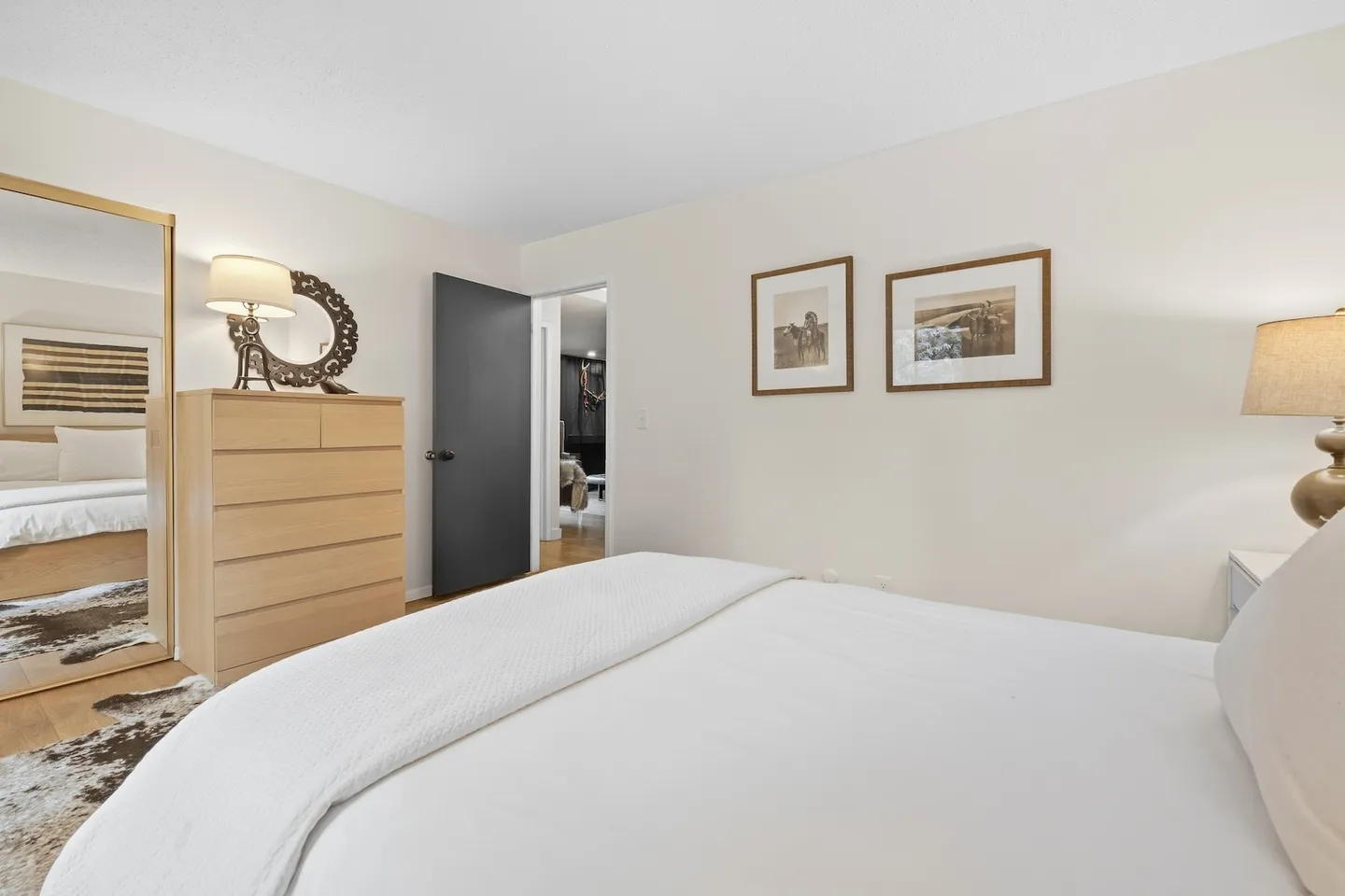 Bedroom featuring a bed with white bedding, a light wood dresser, a full-length mirrored closet door, and an open doorway.