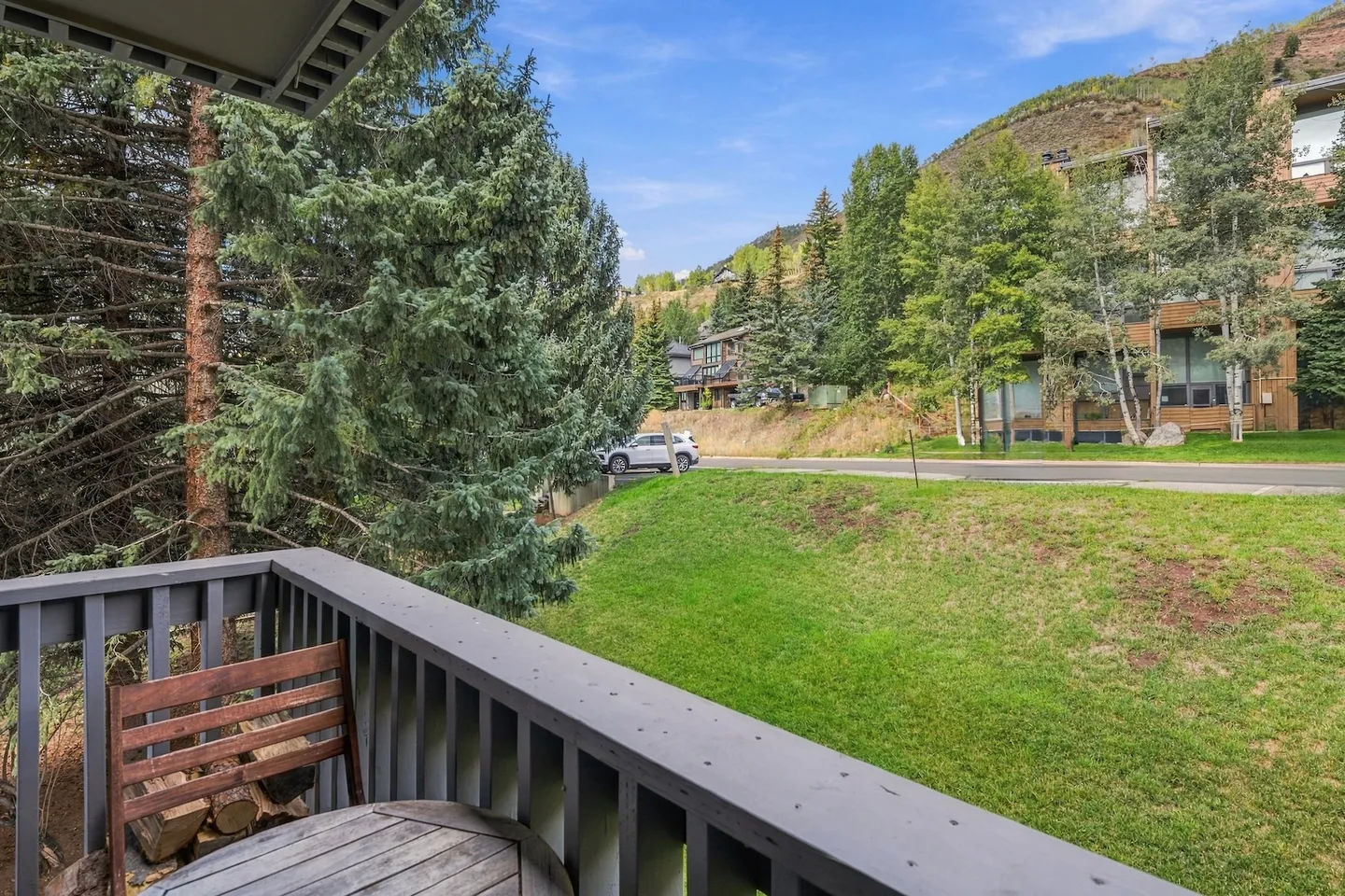 Balcony view overlooking a grassy hill, street, trees, and buildings against a hillside.