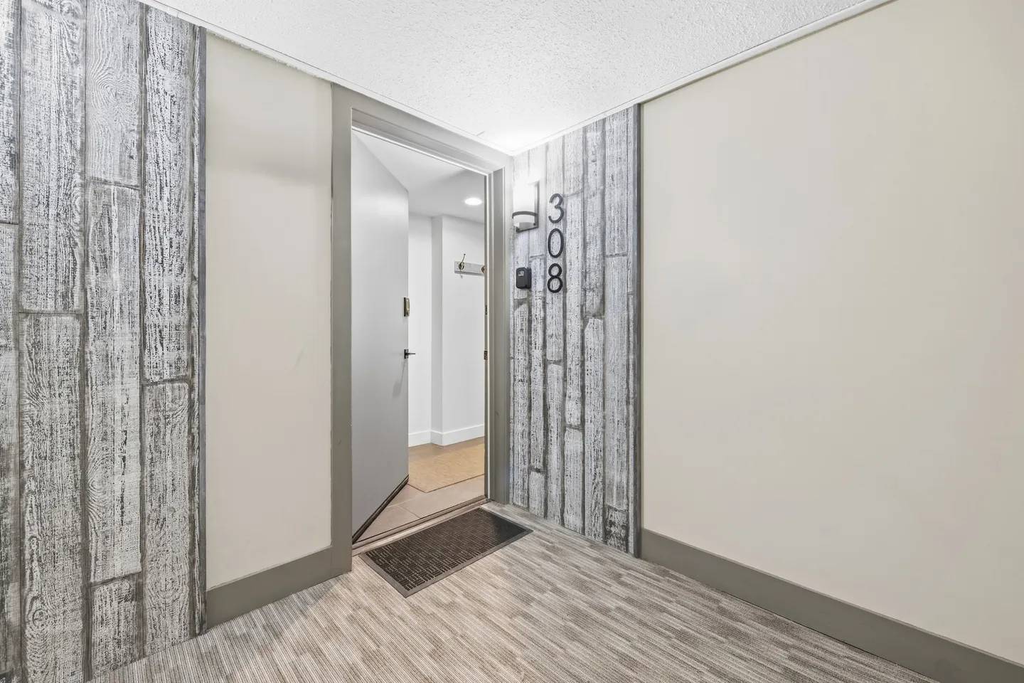 Open unit doorway numbered 308 along an indoor hallway with wood-look plank accent walls.