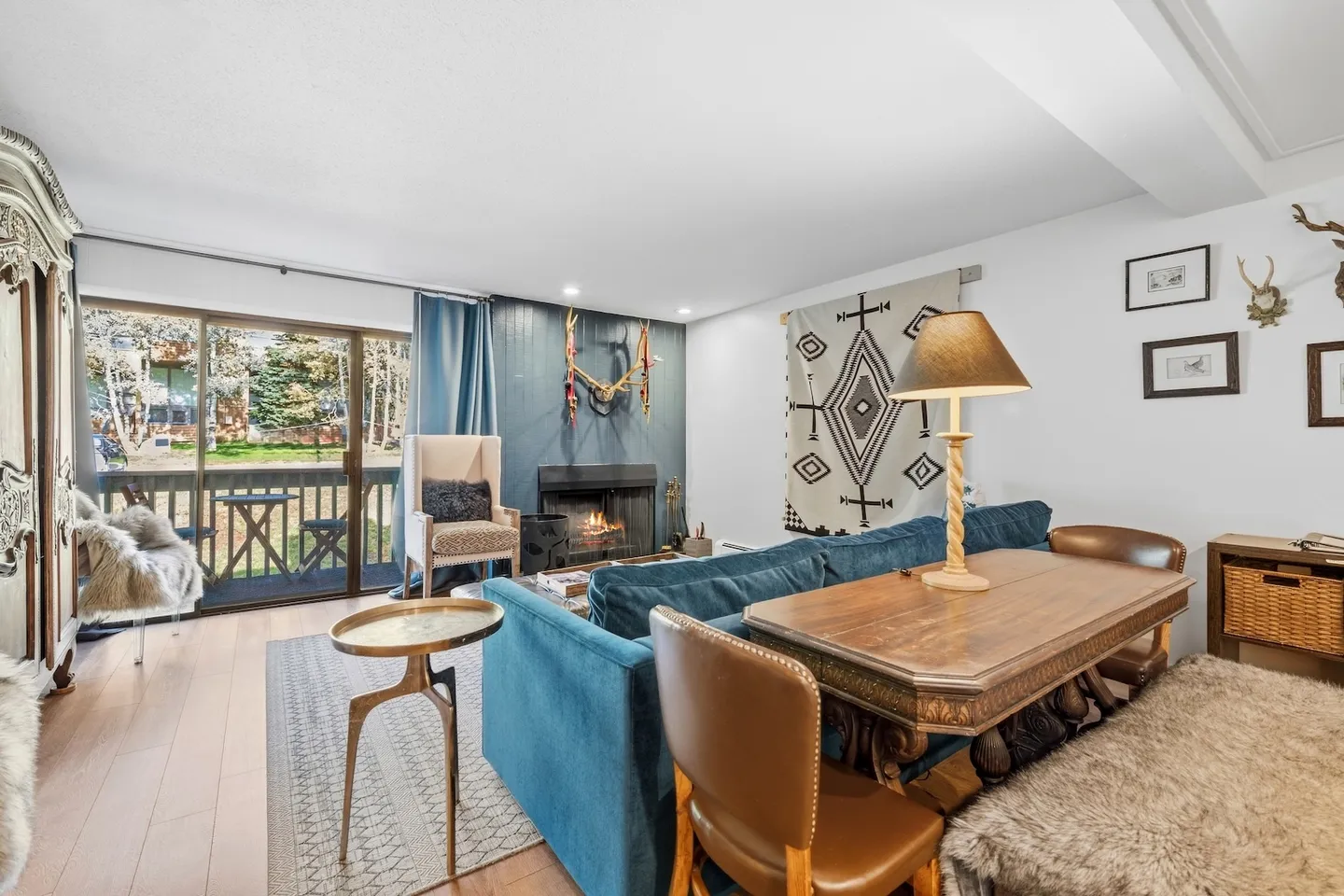 Living and dining space with a blue sofa, dining table, fireplace, and sliding glass door leading to a balcony.