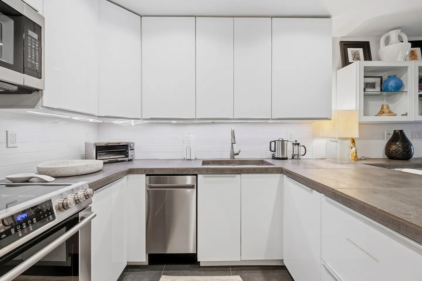 A modern U-shaped kitchen with flat-panel white cabinets, dark countertops, and stainless steel appliances.