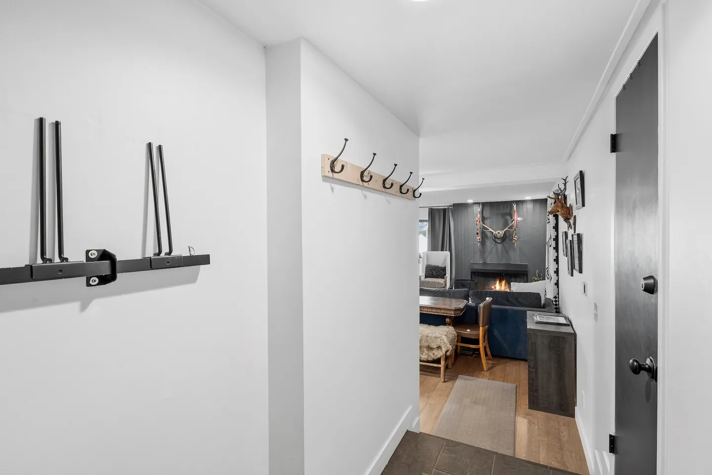 Entryway hallway with wall-mounted coat hooks and ski rack looking toward a living room with a fireplace.