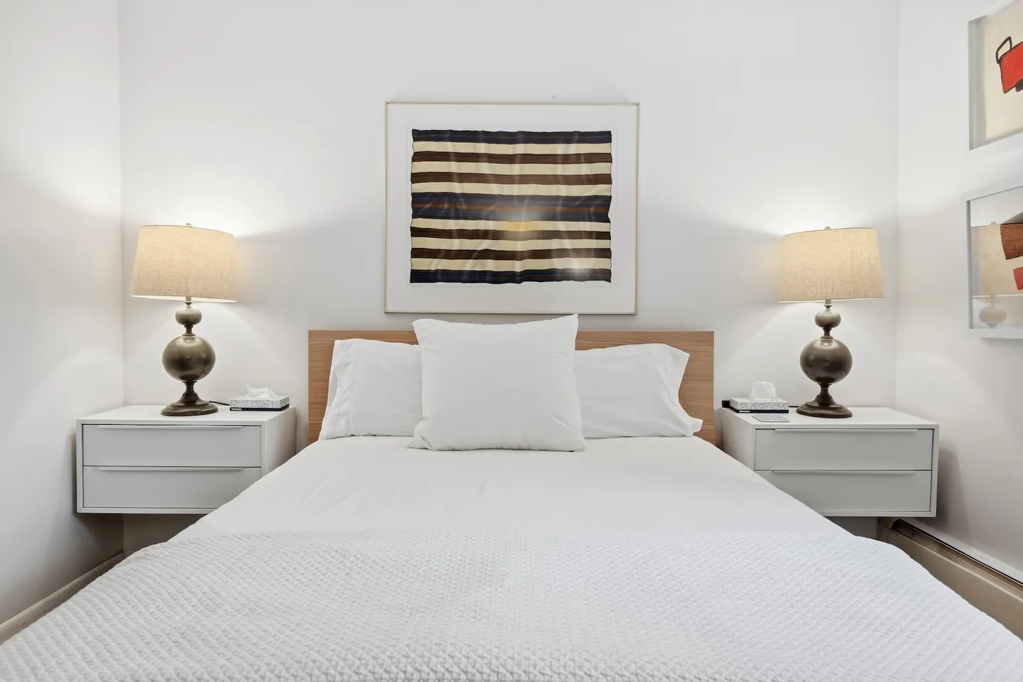 A neatly made bed with white bedding flanked by floating white nightstands and matching lamps.