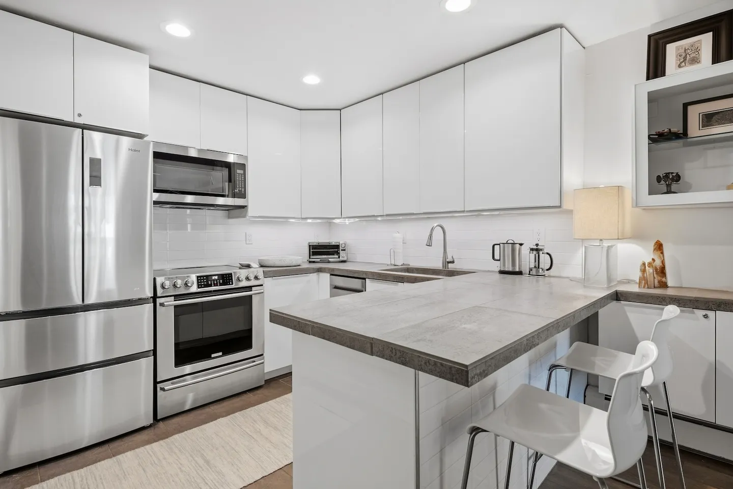 Modern kitchen with white glossy cabinets, stainless steel appliances, and a breakfast bar peninsula with stools.