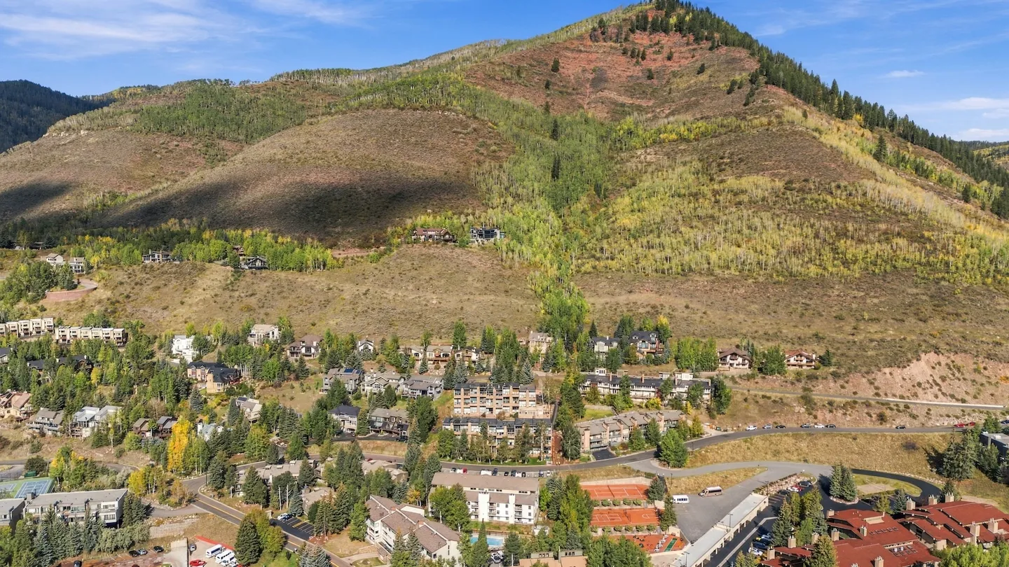 Aerial view of a mountain valley community with houses and condominium complexes nestled at the base of a forested hillside.