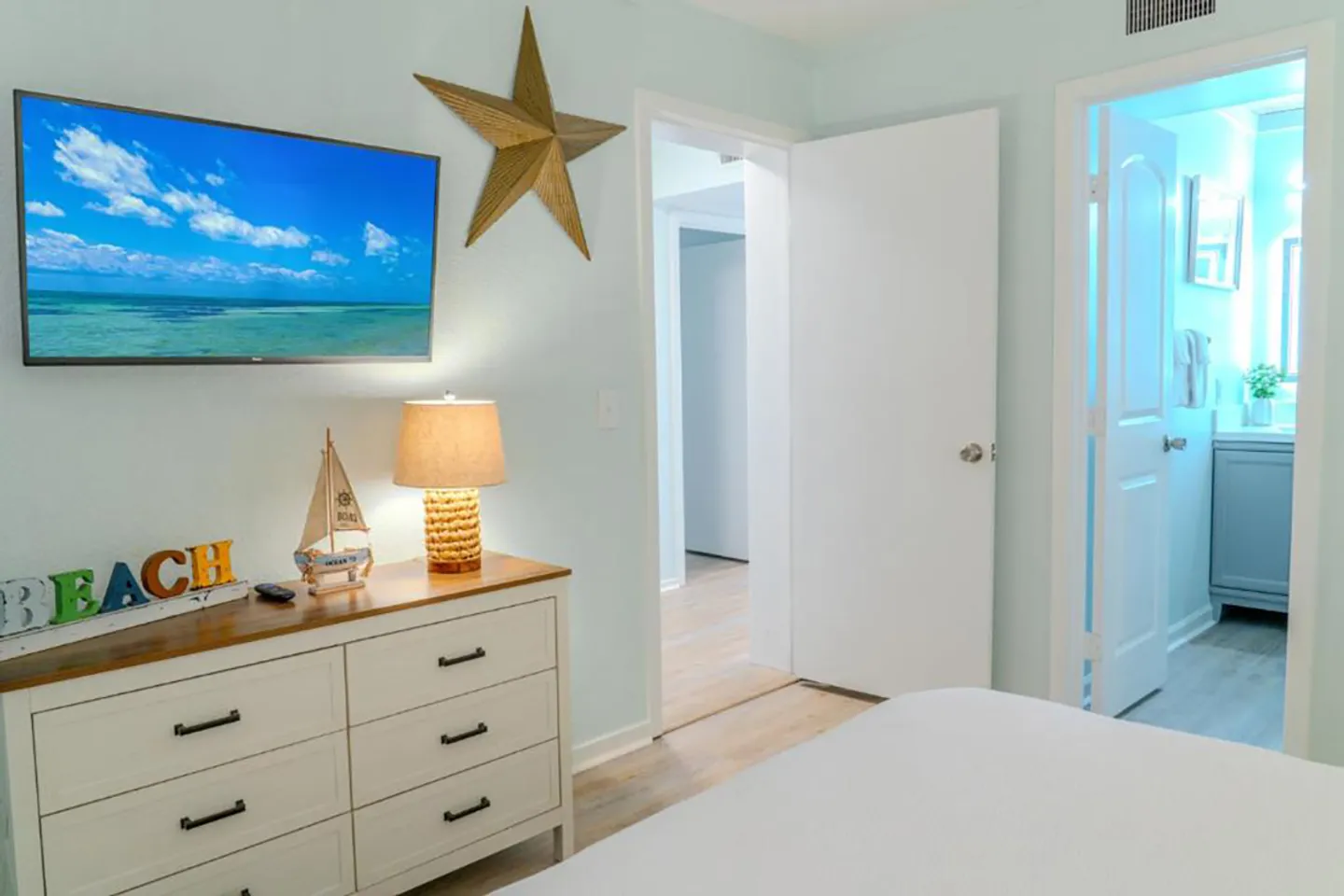 Bedroom featuring a white dresser, wall-mounted television, and doorways leading to a hallway and an ensuite bathroom.
