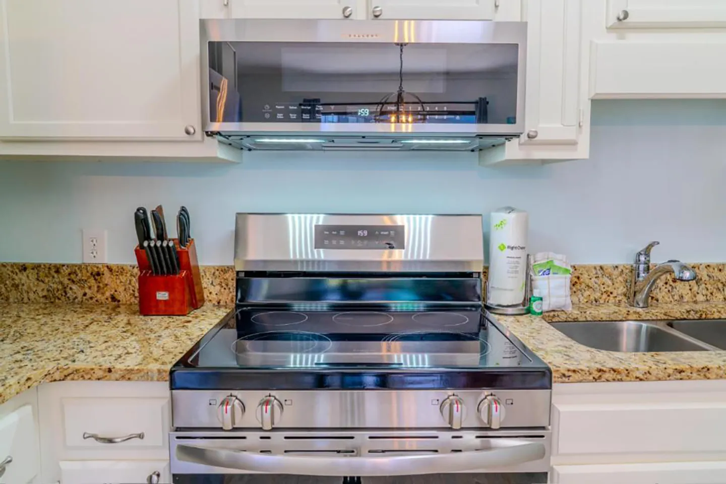 Stainless steel electric range and over-the-range microwave flanked by granite countertops and white cabinetry.
