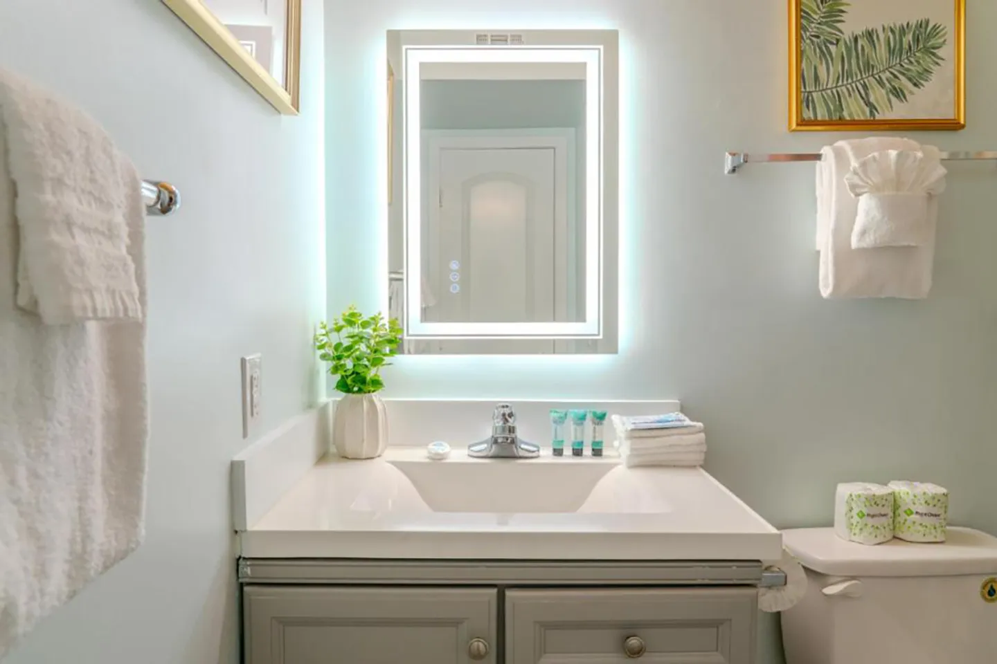 Bathroom vanity with an illuminated LED mirror, white sink, and gray cabinetry.