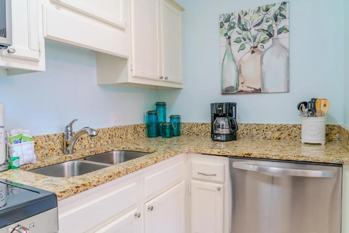 Kitchen corner with white cabinets, speckled granite countertops, a double stainless steel sink, and a stainless steel dishwasher.