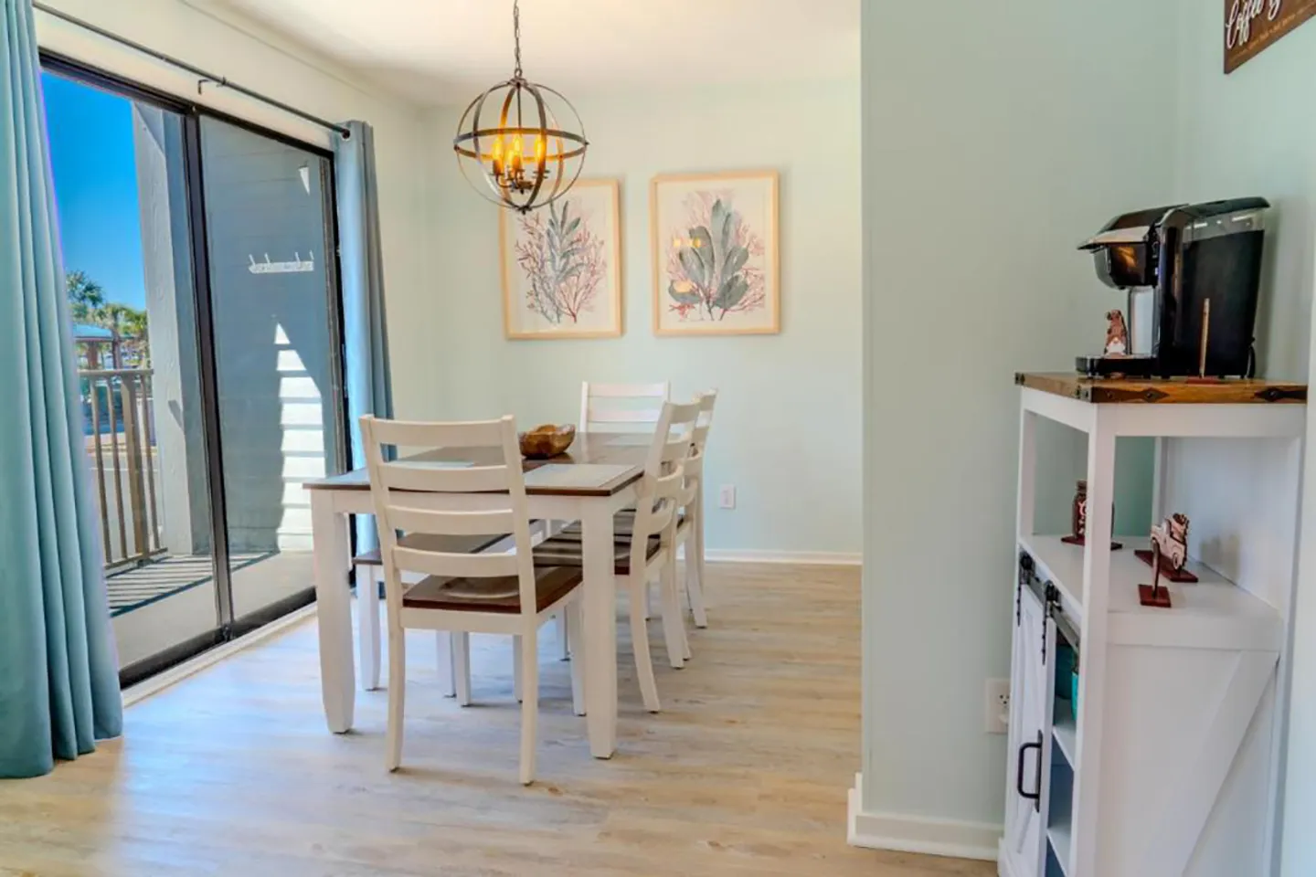 Dining area with a wooden table and white chairs next to sliding glass doors.