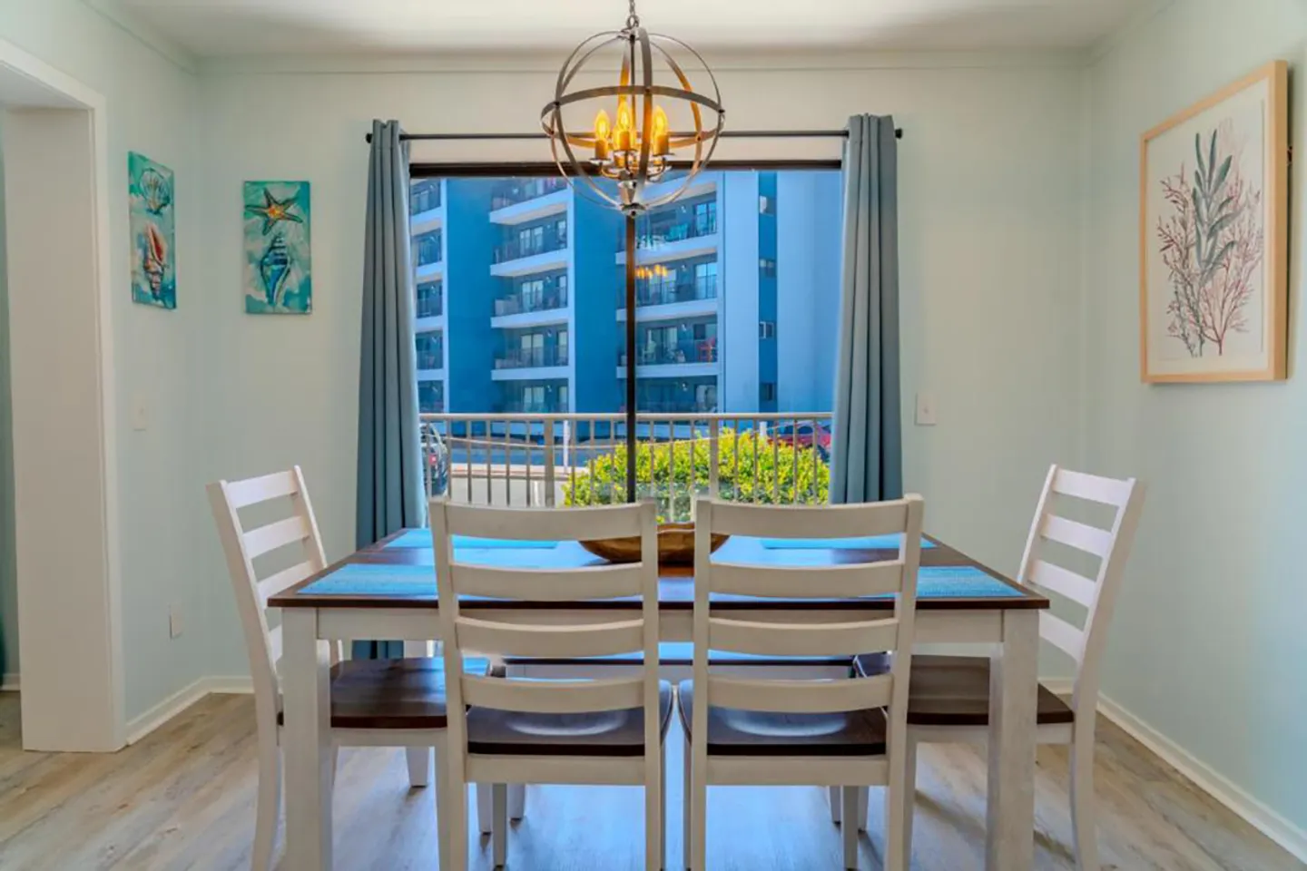 Dining table and chairs centered in front of a sliding glass door with a chandelier overhead.