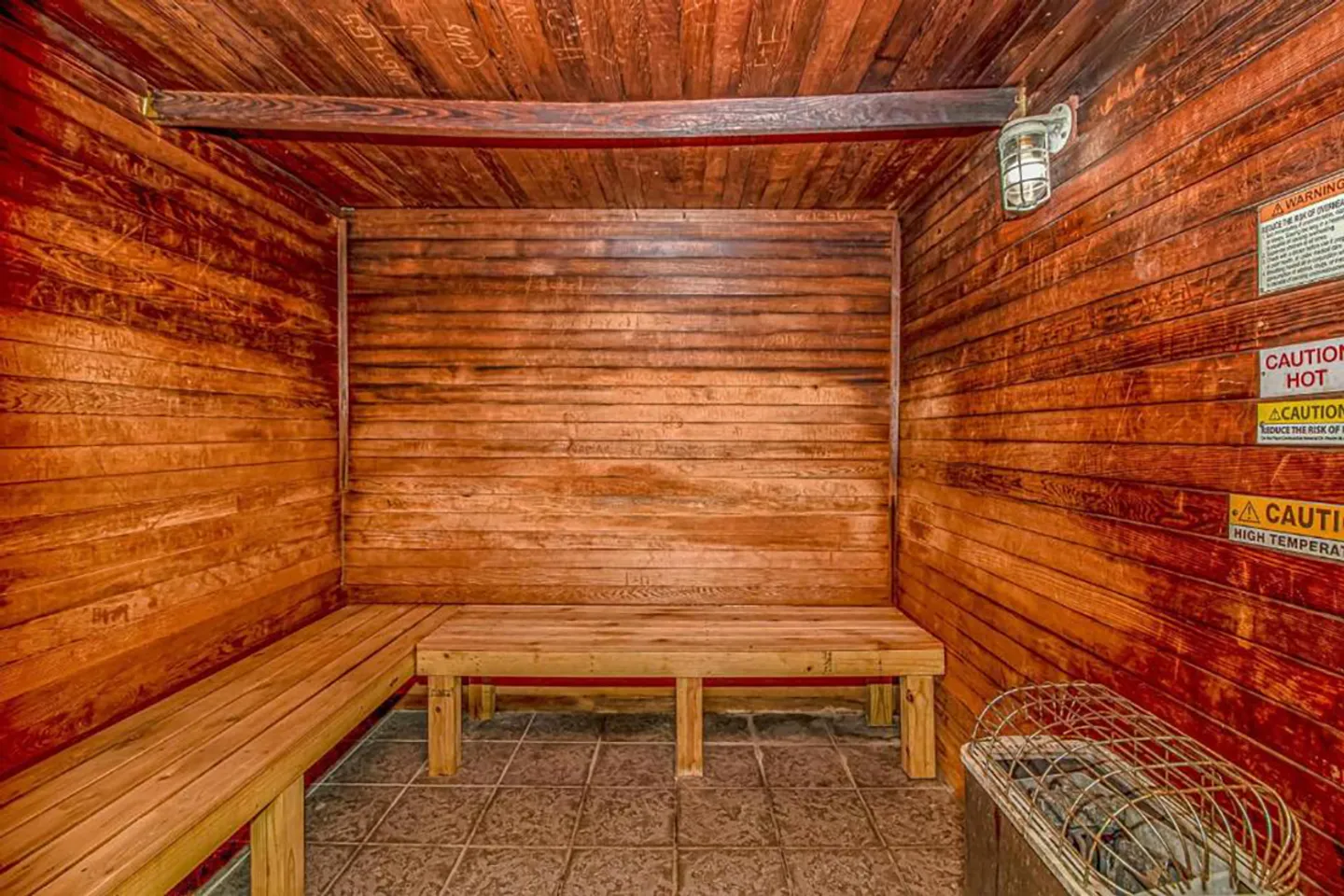 Indoor wood-paneled sauna with wooden benches, tiled floor, and a sauna heater.