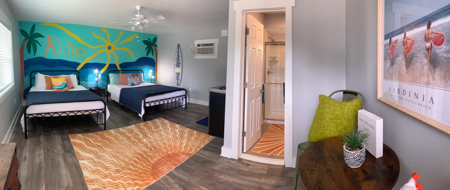 Bedroom featuring two beds under a painted tropical wall mural, wood-look flooring, and an open doorway to an en suite bathroom.