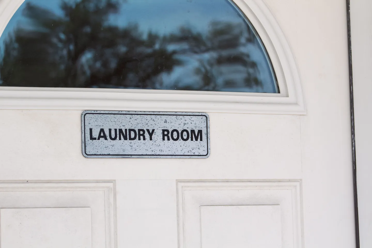 Close-up of a white door with an arched glass insert and a sign labeled LAUNDRY ROOM.