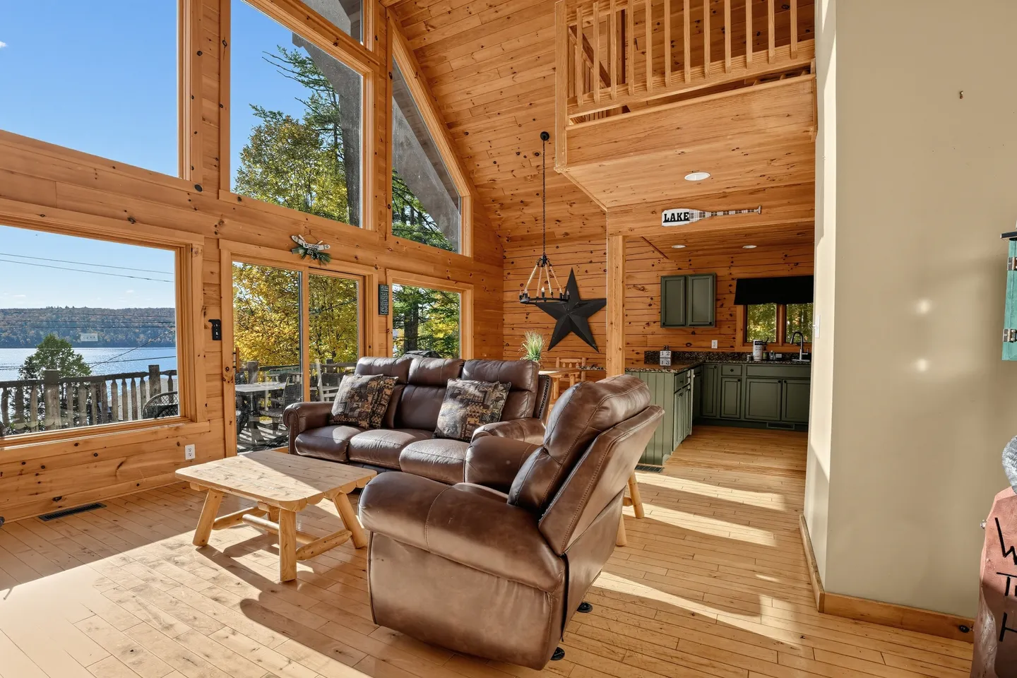 Living room with wood-paneled walls and ceiling, brown leather reclining seating, and large windows overlooking a lake.