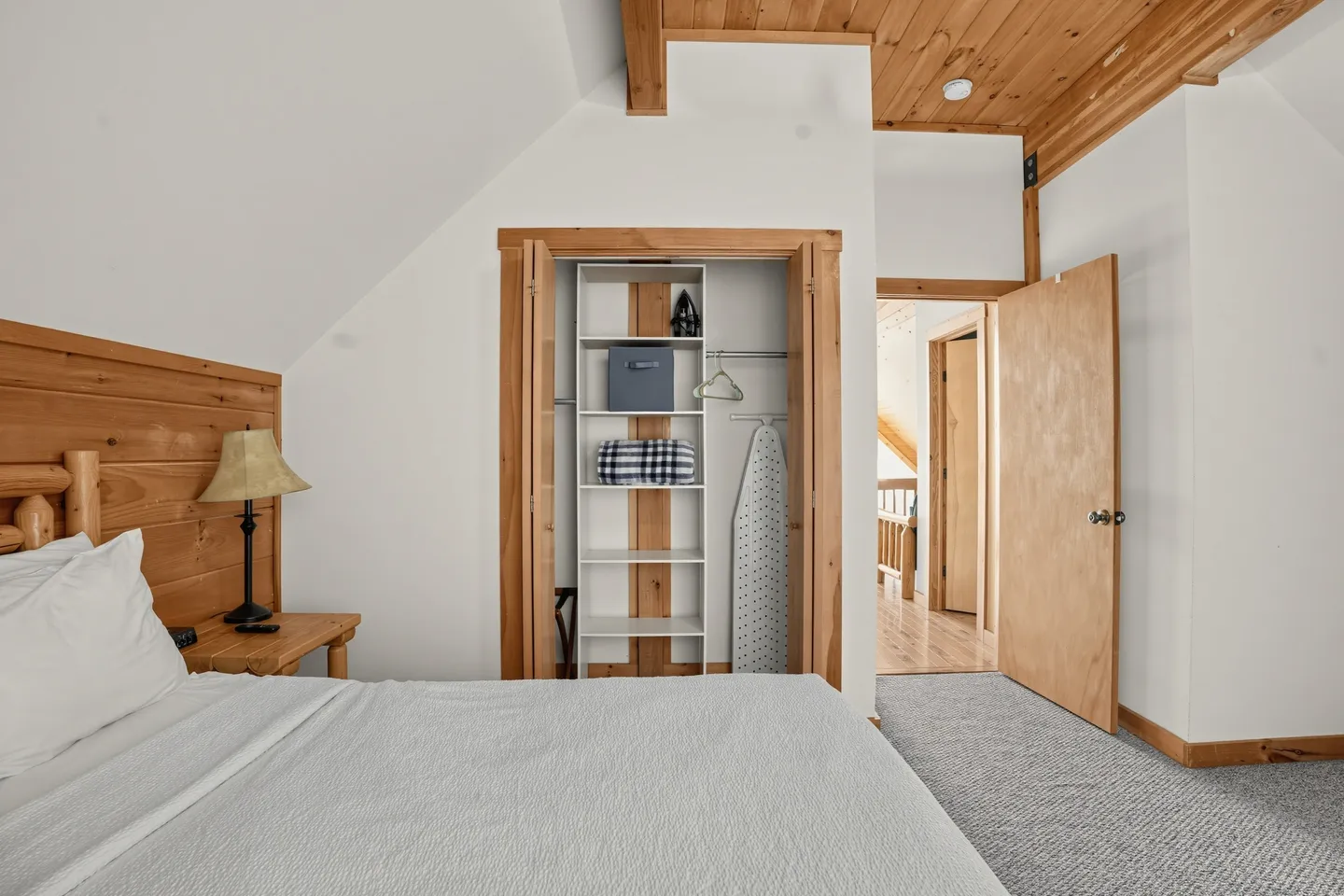 Bedroom with an open closet featuring shelving, an iron, and an ironing board, alongside a log-style bed and wooden ceiling.