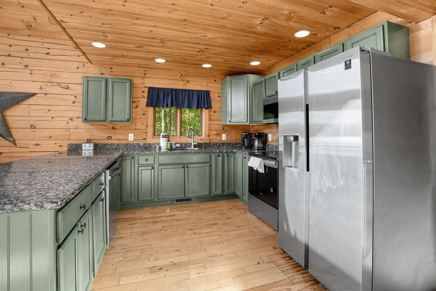 Kitchen with sage green cabinets, speckled granite countertops, wood paneled walls, and stainless steel appliances.