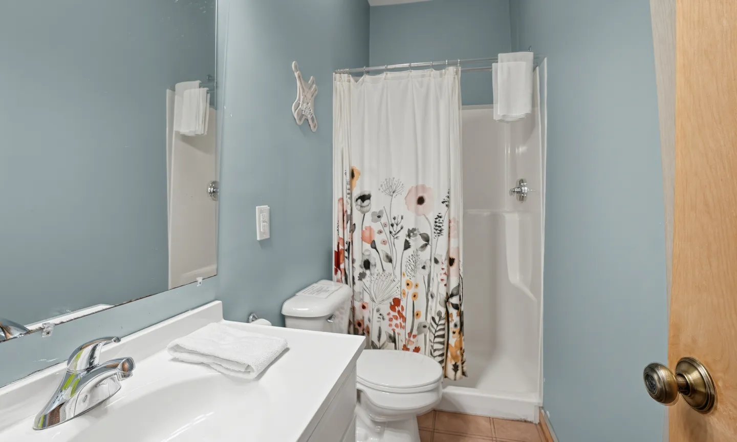Bathroom with a white vanity sink, toilet, and shower stall with a floral curtain.