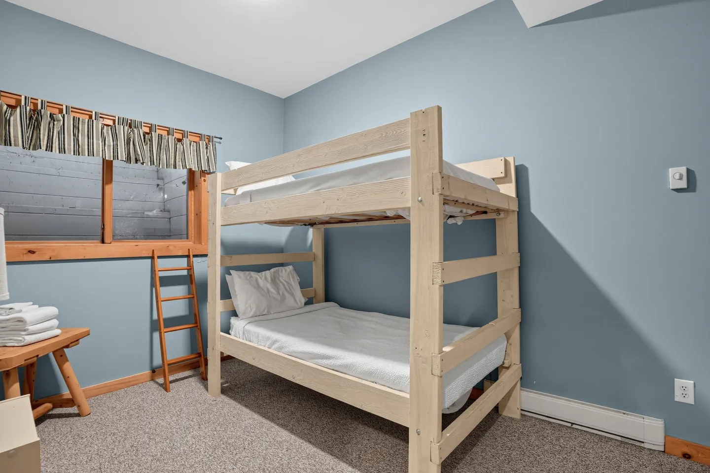 Bedroom with light blue walls, carpeted flooring, and a light wood bunk bed set up with white bedding.